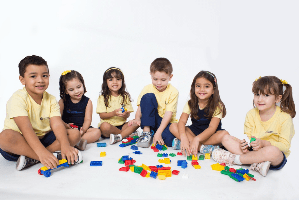 Grupo de alunos uniformizados, sentado em meio círculo brincando com peças de Lego ADQUIRINDO COMPETÊNCIAS SOCIOEMOCIONAIS