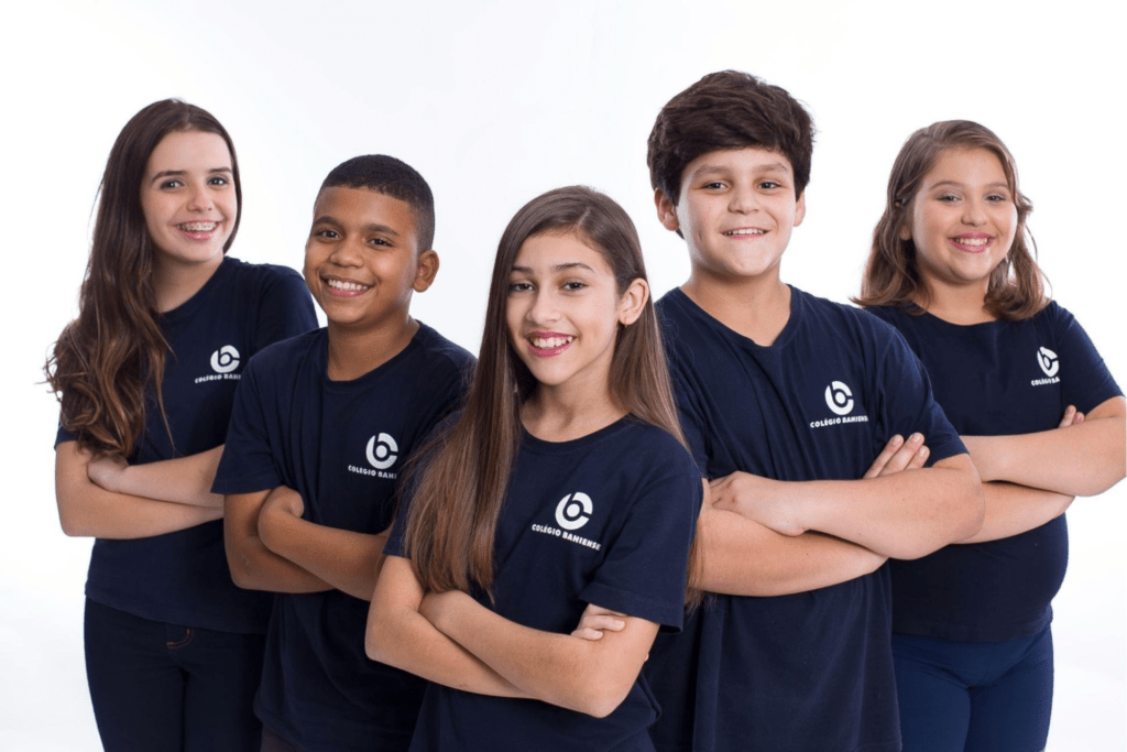 Grupo com cinco alunos do ensino fundamental do colégio que preza pelas habilidades socioemocionais, uniformizados e posando para a foto sorrindo.