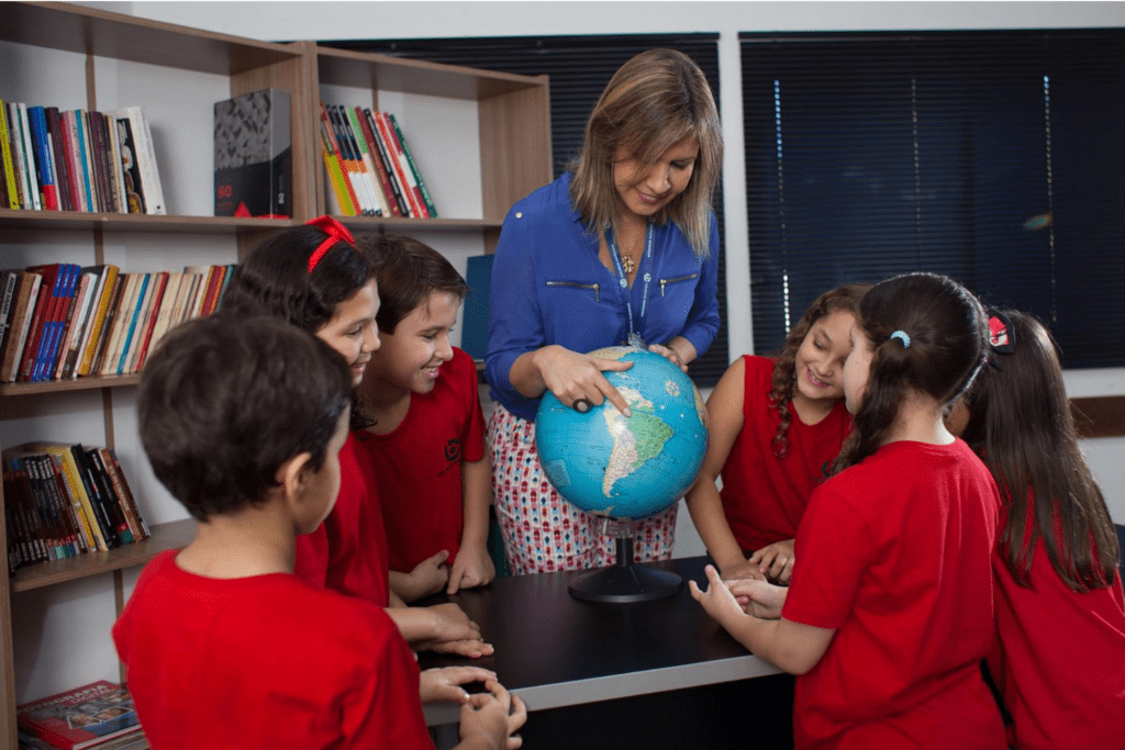 Alunos em sala de aula olhando o Globo Terrestre junto com a professora