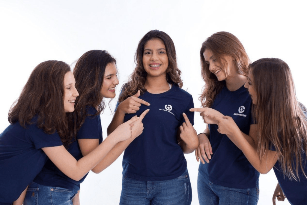 Grupo com cinco estudantes vestindo o uniforme Colégio Bahiense, apontando para o logo da escola da adolescente focalizado no centro da foto