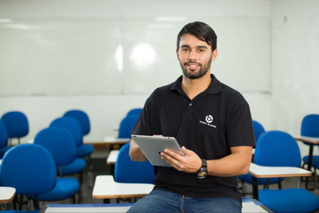 Professor do Colégio Bahiense em sala de aula segurando um caderno de anotações e olhando para a câmera