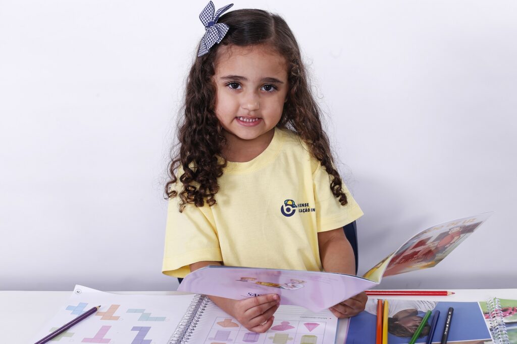 Aluna da Educação Infantil com um livro nas mãos e praticando a leitura na infância