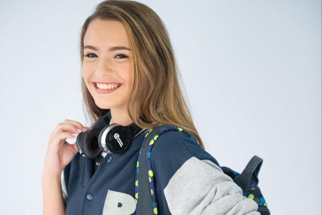 menina feliz com fone de ouvido e mochila escolar