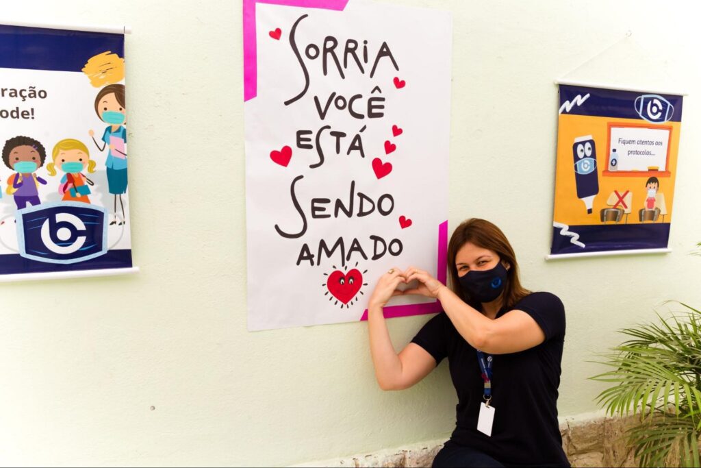 Professora e cartaz “sorria, você está sendo amado”.