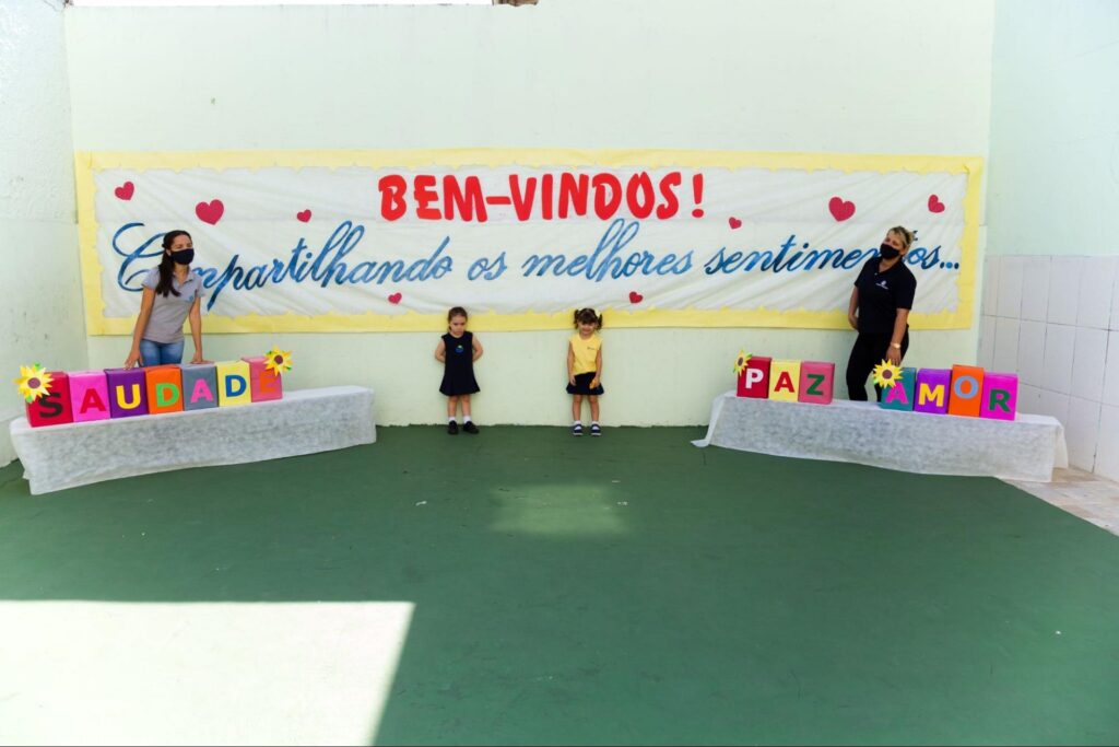 Educação acolhedora: professores e alunos com cartaz “bem-vindos, compartilhando os melhores sentimentos”.