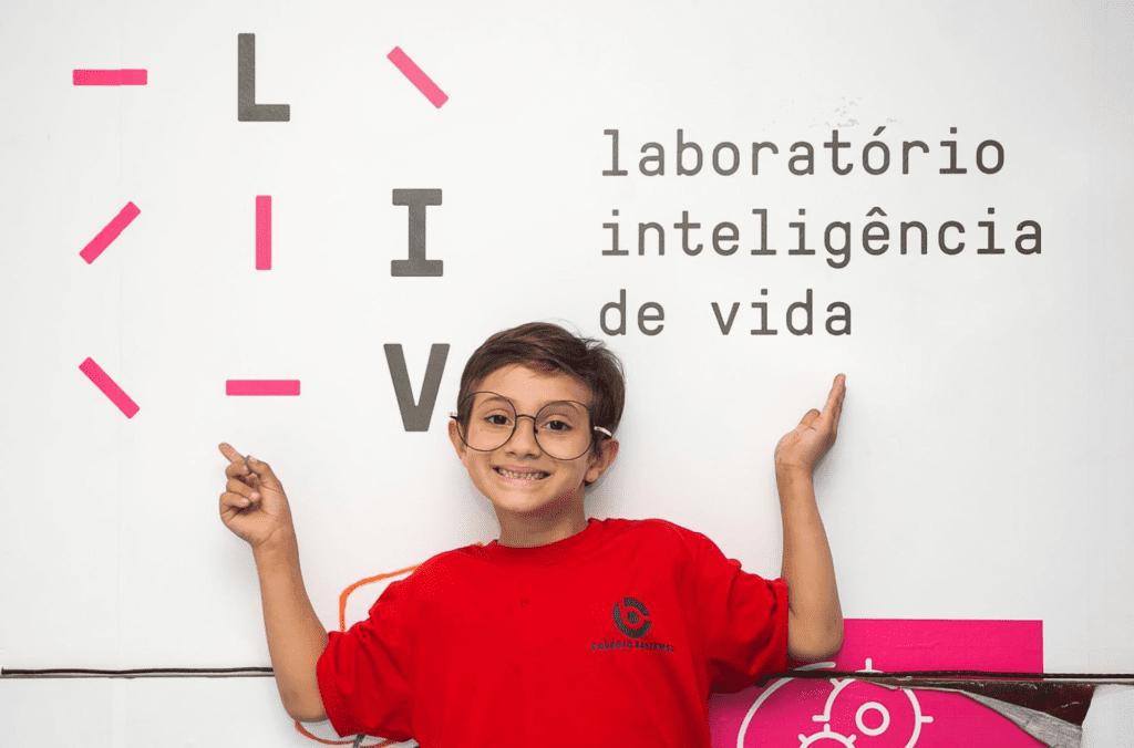 Criança posando em frente ao banner do Laboratório de Inteligência de Vida (LIV)