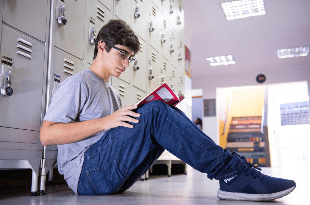 Aluno do colégio bilíngue sentado no chão estudando