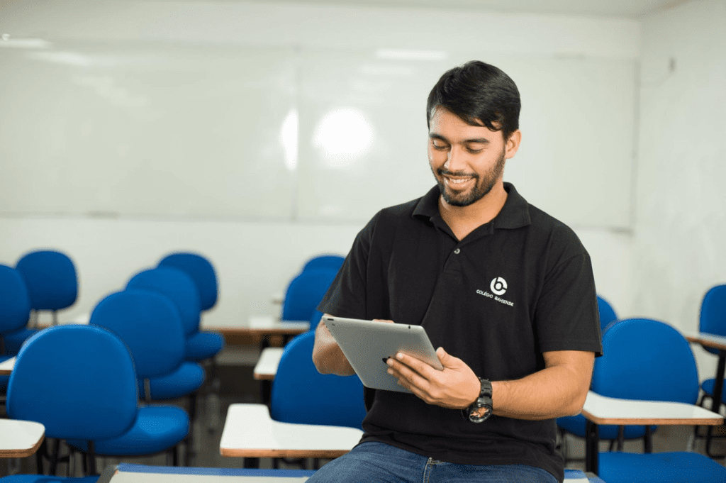 Professor do Colégio Bahiense sentado em sala de aula segurando um tablet