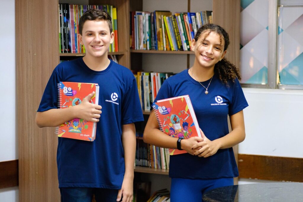 Alunos do ensino bilíngue do Colégio Bahiense uniformizados posando para foto em frente a uma estante cheia de livros