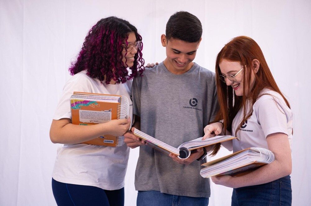 Três alunos do Colégio Bahiense uniformizados posando para foto enquanto olham anotações em caderno