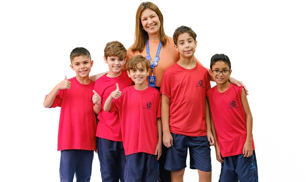 Alunos do Colégio Bahiense em pé uniformizados posando para foto com professora